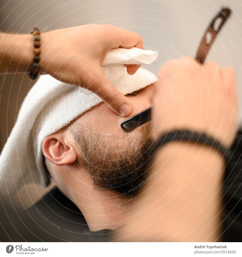A barber shaves the cheek of a bearded customer with a dangerous razor. Shaving the contour of the beard for the right shape. Beard Blade Cheek Shaven Modern