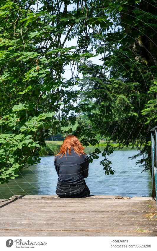 A woman from behind, sitting on a wooden pier by the lake women Teenager depressed enjoy Redhead backgrund think depression summer girl tree alone black