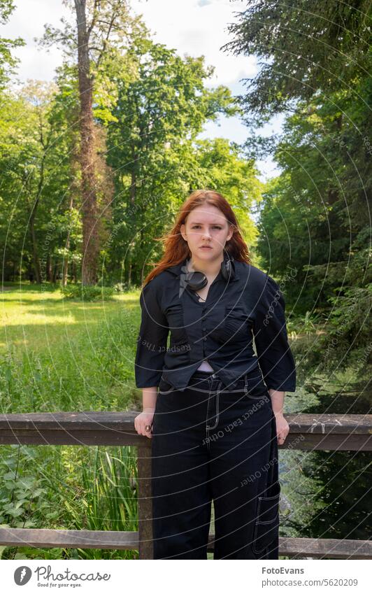 A red-haired women  stands at the railing of a bridge in nature wood copy space lonely depressed back Redhead backgrund day thoughtful think enjoy landscape