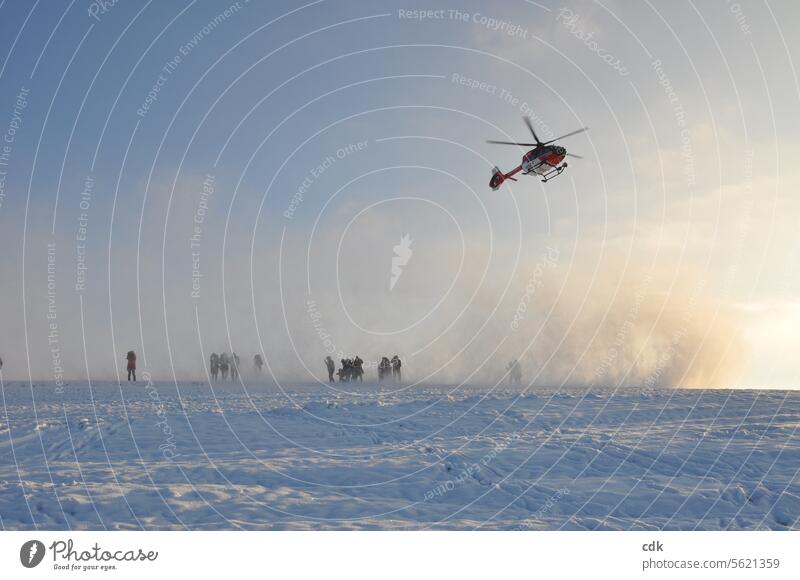 Out of nowhere, an air rescue helicopter suddenly appears in the sky and envelops people in a swirl of fresh snow as it lands. Helicopter Technology Aviation