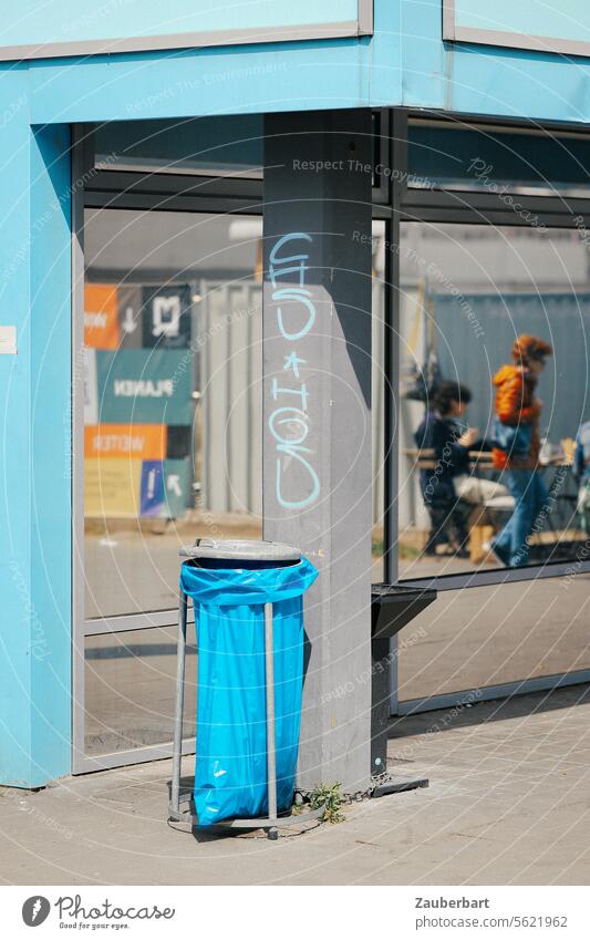 Corner of a house in light blue, garbage bag in blue, glass facade and mirrored person, urban street scene House (Residential Structure) Blue Bin bag holder