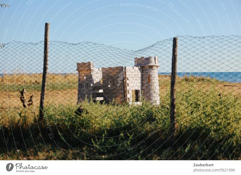 A play castle on the beach, a fence in front of it, curious and puzzling Play castle beach castle Ocean Fence quaint Longing questionable vacation Castle
