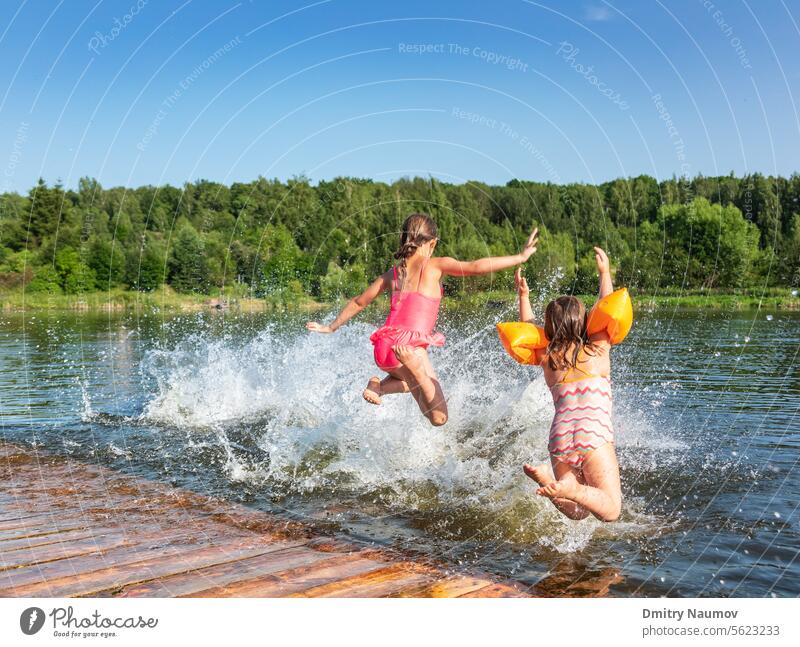 Happy little girls having fun playing in a lake jumping into water during summer holidays Lakeshore activity carefree child childhood children enjoy enjoyment