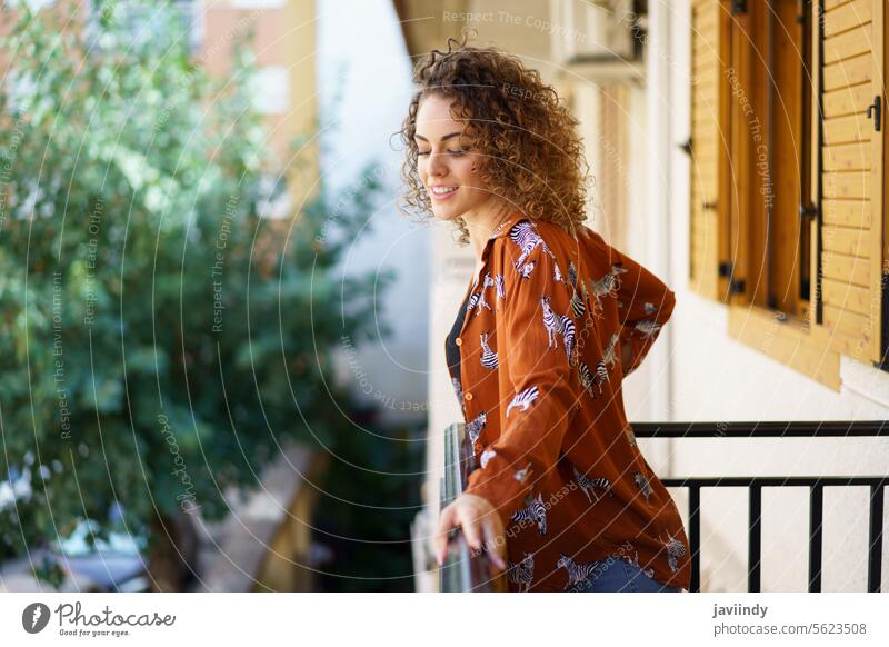 Happy young woman in casual wear with curly hair standing on balcony smile positive cheerful happy charming optimist glad female appearance pleasant outfit