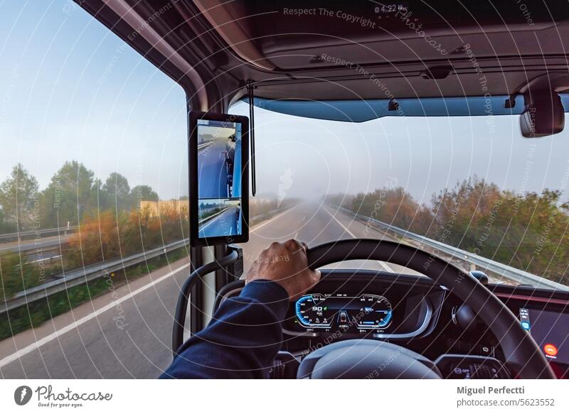 View from the inside of the cabin of a truck on a highway with fog, truck with rearview camera and screen. dashboard rear view road driver hand steering wheel