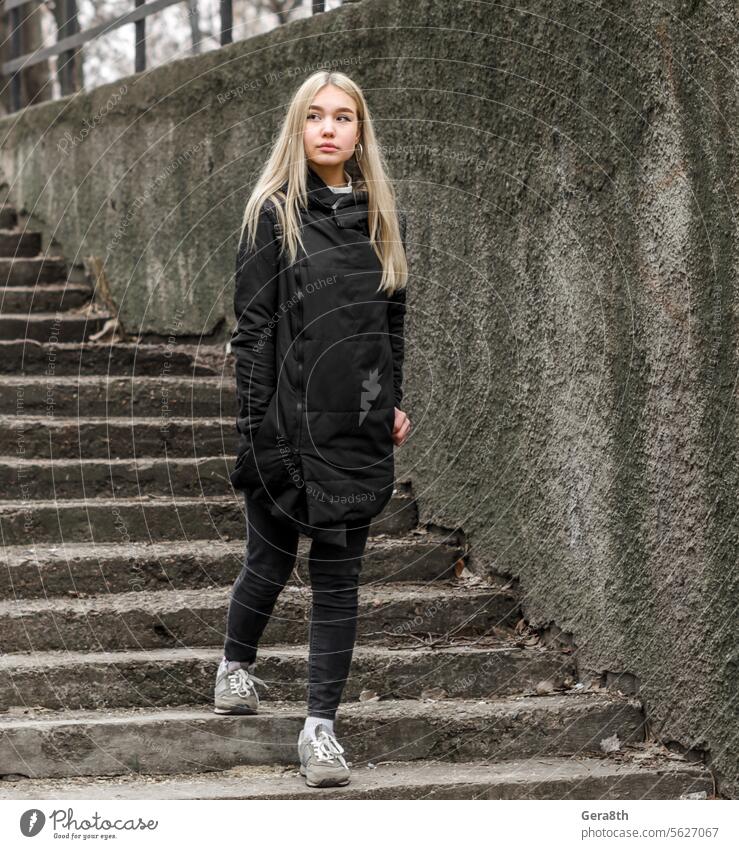 young girl with blond hair in black clothes comes down the stone stairs adult autumn blonde city dreamy erase girl blonde gray hairstyle look modern pensive