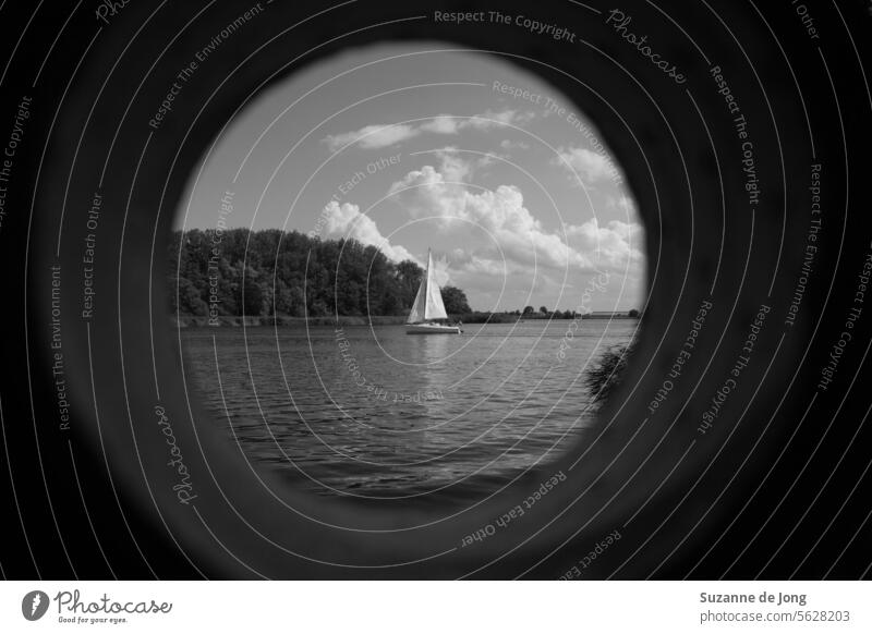 black and white image of a sail boat in a lake with a cloudy sky, viewed through (fake) binoculars Binoculars sailing ship water Sailboat Sailing ship Water