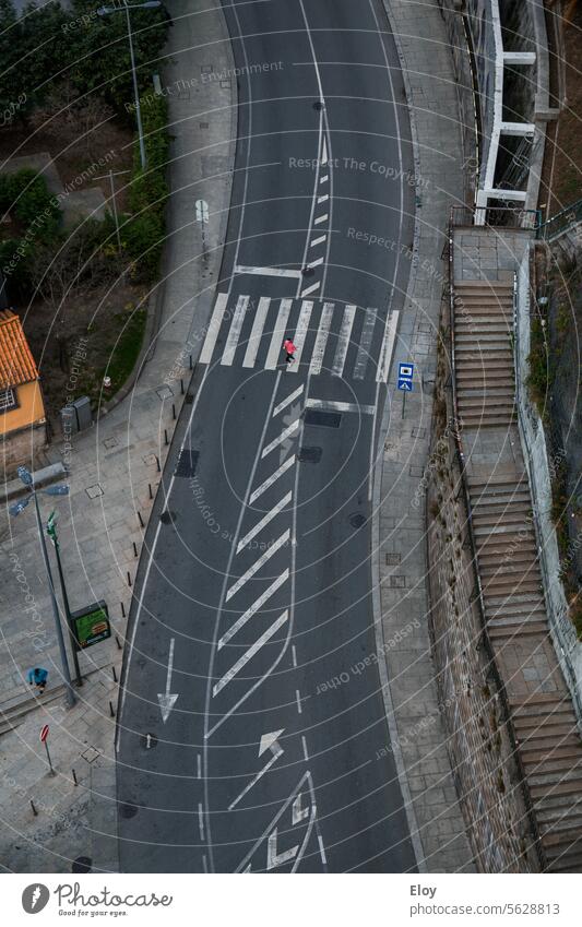 road, aerial shot, there is a pedestrian crossing the road, on one side you can see a long staircase and on the other a sidewalk, you can only see one person and there are no cars