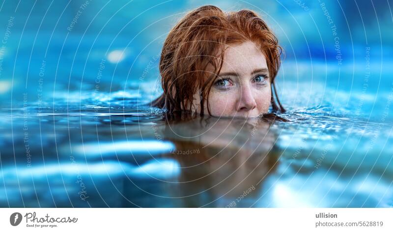 portrait of swimming sexy, young red haired woman with freckles and red wet hair, in turquoise spa pool water, head half under water redhead copy space joy