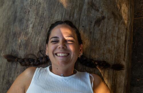 smiling young woman, close-up of a brunette woman with two braids, smiling with her eyes closed lying on a wooden log Smiling Adults 18 - 30 years Young woman