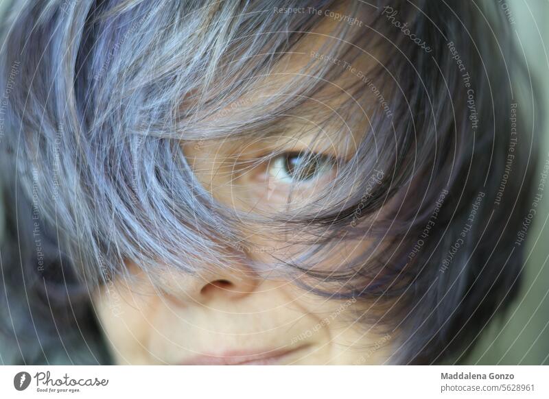 Portrait of a woman with face mostly covered by her hair portrait hairstyle wind purple silver grey dark eye older wrinkle smirk smile female person mature age
