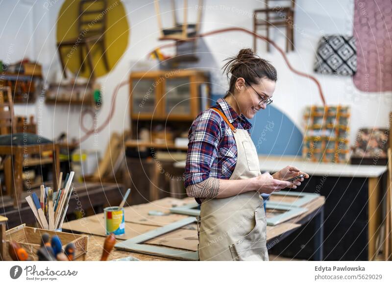 Portrait of young female carpenter using mobile phone in her workshop Furniture Carpenter Restoring Carpentry wood Chair building Manufacturing Craft Renovation