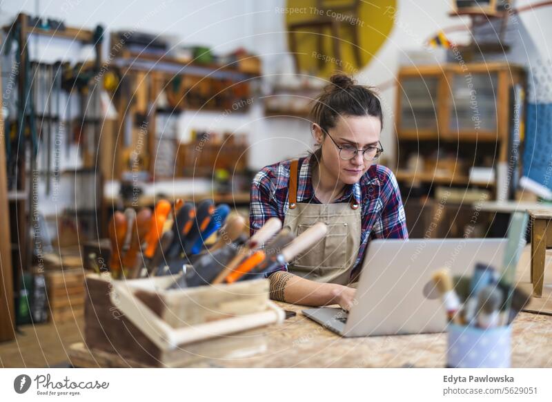Young craftswoman using laptop in her workshop Furniture Carpenter restoring Joiners workshop Wood Chair Building Production Craft (trade) Renovation repairing