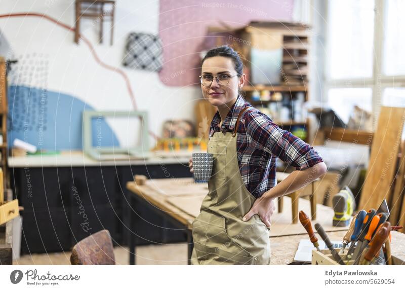 Portrait of a young female carpenter holding a cup of coffee in her workshop Furniture Carpenter Restoring Carpentry wood Chair building Manufacturing Craft