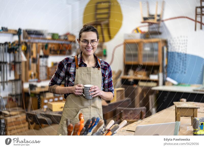 Portrait of a young female carpenter holding a cup of coffee in her workshop Furniture Carpenter Restoring Carpentry wood Chair building Manufacturing Craft