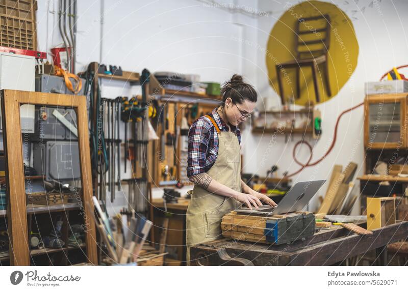 Young craftswoman using laptop in her workshop Furniture Carpenter restoring Joiners workshop Wood Chair Building Production Craft (trade) Renovation repairing