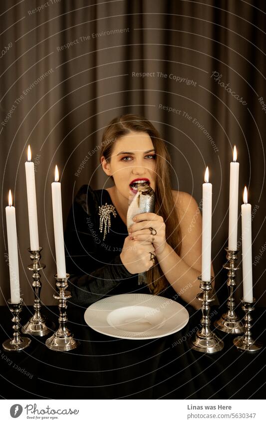 It’s Christmas Eve and a gorgeous brunette girl is eating raw herring like a beast. A pretty beast with some makeup and candlelight surrounded her in a restaurant. The air is filled with holiday cheer as this elegant woman revels in the joyful atmosphere.