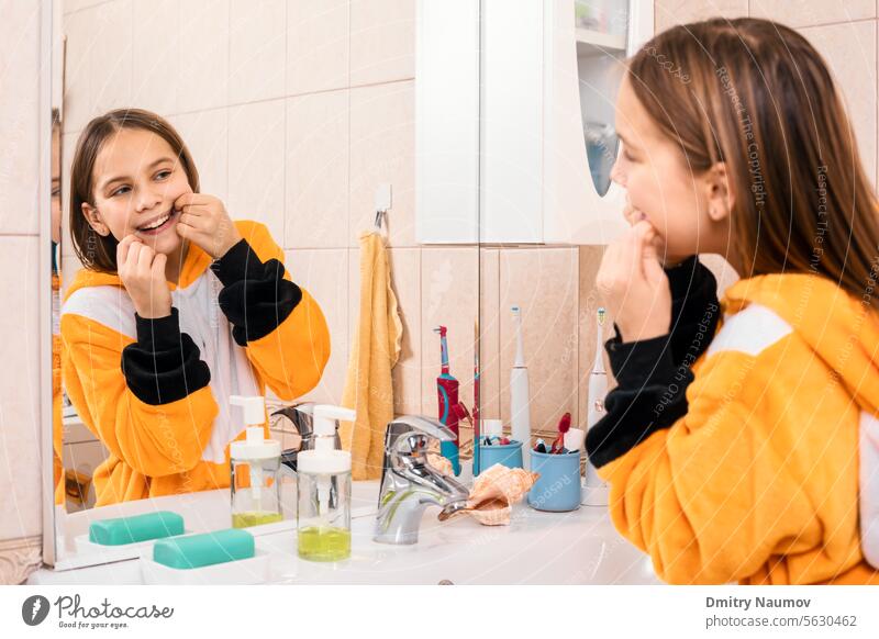 Tween girl wearing orange pyjamas uses dental floss to remove plaque between teeth Healthy Lifestyle Pajamas bathroom bedtime care caries child childhood