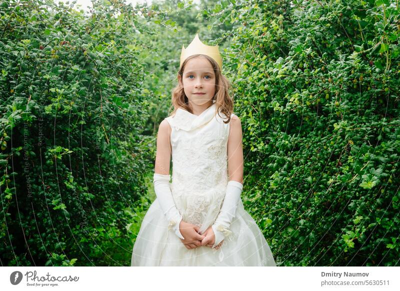 Outdoor portrait of elementary age girl wearng princess dress and paper crown standing in wet garden looking at camera Looking At Camera adorable beautiful