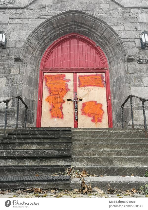 boarded up door of abandoned church with cancelled graffiti and locked with a chain red old vandalized steps stairs building architechture ruined street cement
