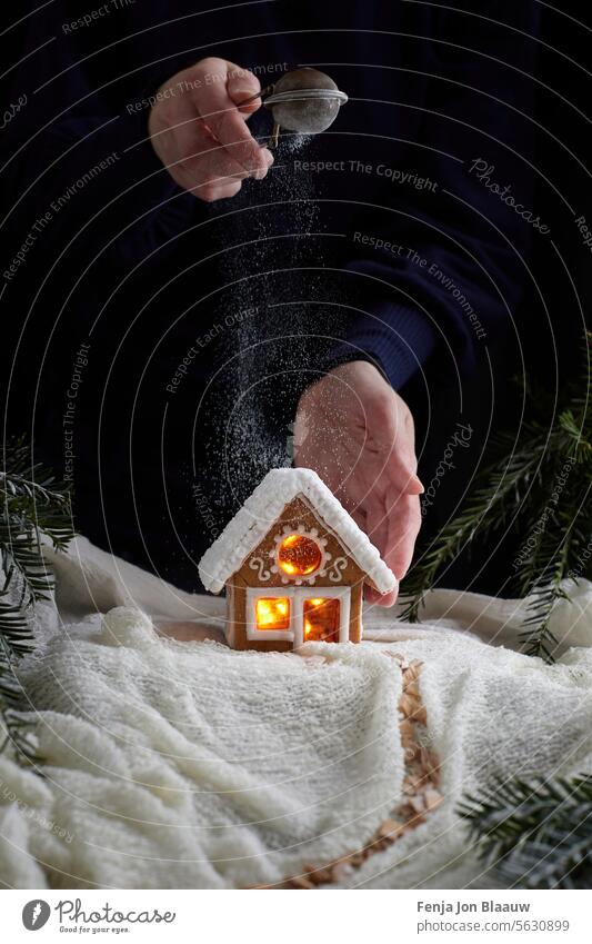 Sprinkling sugar on homemade gingerbread house in a winter wonderland christmas setting person december white moody moody food scene food styling snow cookies