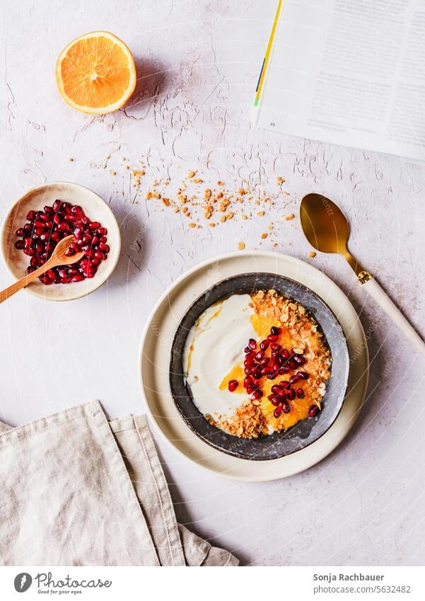 A bowl of muesli, yogurt and fruit on a table. Top view. Breakfast Cereal Yoghurt Fruit Diet Orange Pomegranate Oat flakes Bowl Food Morning Table plan Gray