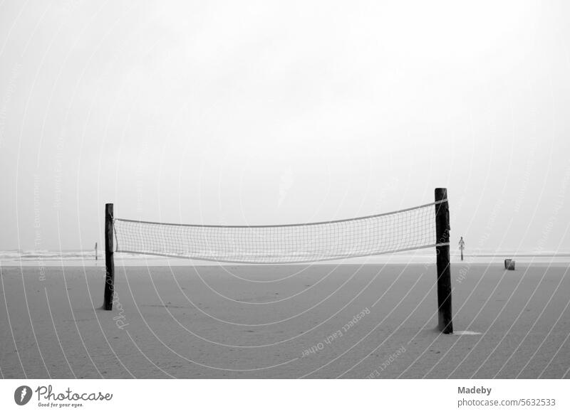 Volleyball net for beach volleyball in rain and storm at the beach playground on the beach of St. Peter-Ording in the district of Nordfriesland in Schleswig-Holstein in autumn on the North Sea coast in black and white