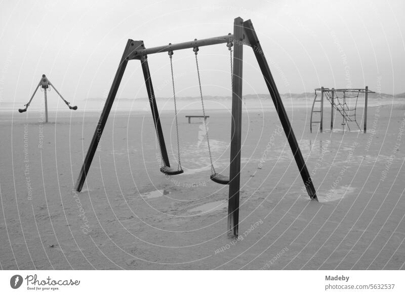 Abandoned playground equipment with bench in the rain and storm at the beach playground on the beach of St. Peter-Ording in the district of Nordfriesland in Schleswig-Holstein in the fall on the North Sea coast in black and white