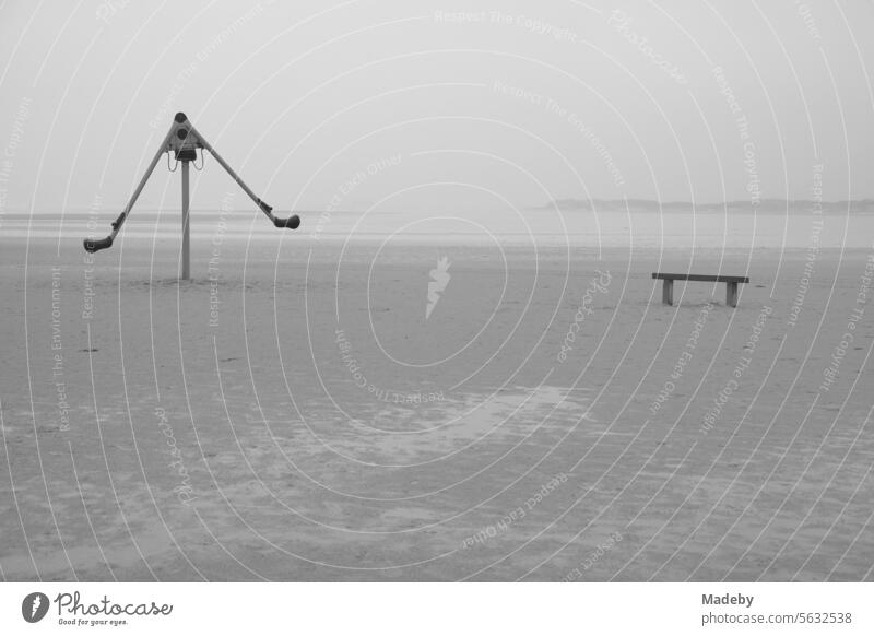 Abandoned playground equipment with bench in rain and storm at the beach playground on the beach of St. Peter-Ording in the district of Nordfriesland in Schleswig-Holstein in the fall on the North Sea coast in black and white