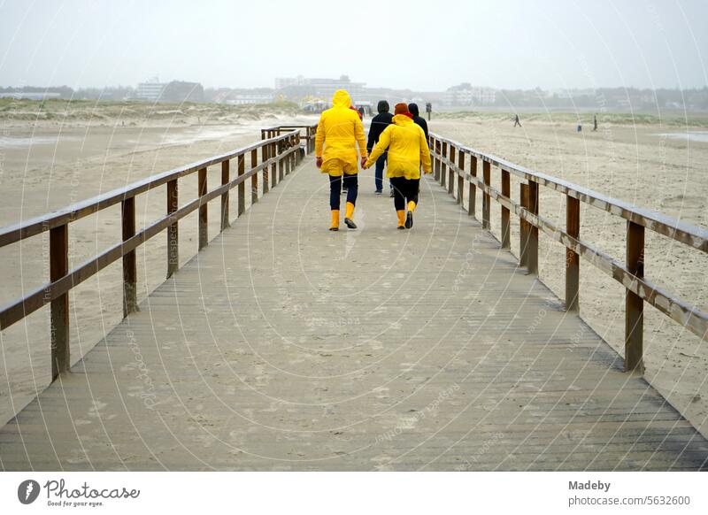 Tourists in yellow East Frisian mink in stormy and rainy weather on the pier on the beach of St. Peter-Ording in the district of Nordfriesland in Schleswig-Holstein in the fall on the North Sea coast