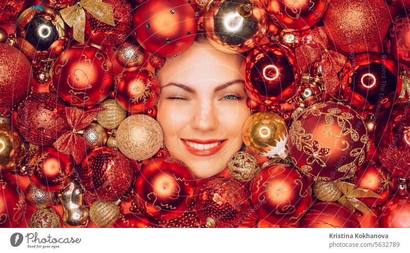 Happy woman winked with joy smile in red Christmas tree toys balls. Holidays. christmas tree new year decoration holiday home ornament shiny decorate gift light