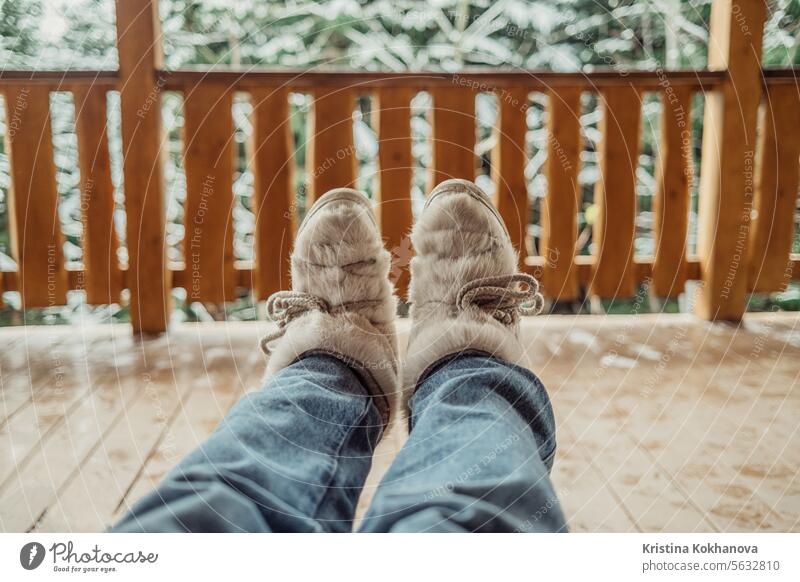Woman legs in winter shoes - fur trendy boots on wooden balcony background. fashion female leather modern warm wear white comfortable elegant isolated new