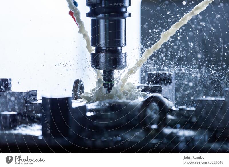 Close-up view of vertical cnc steel milling process with external water coolant streams, splashes and a lot of metal chips, high contrast industrial flood