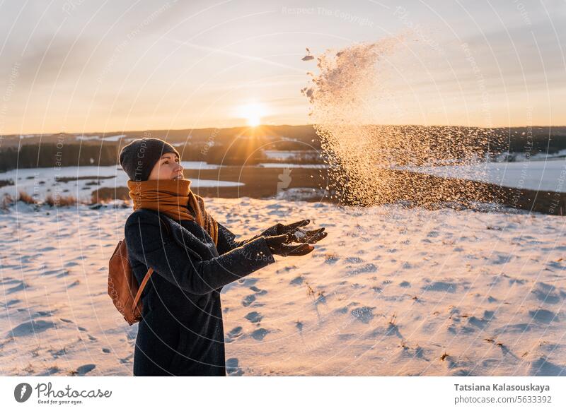 A woman in winter in warm clothes throws her palms and snow against the background of sunset female toss people person European White adult mid adult hold one