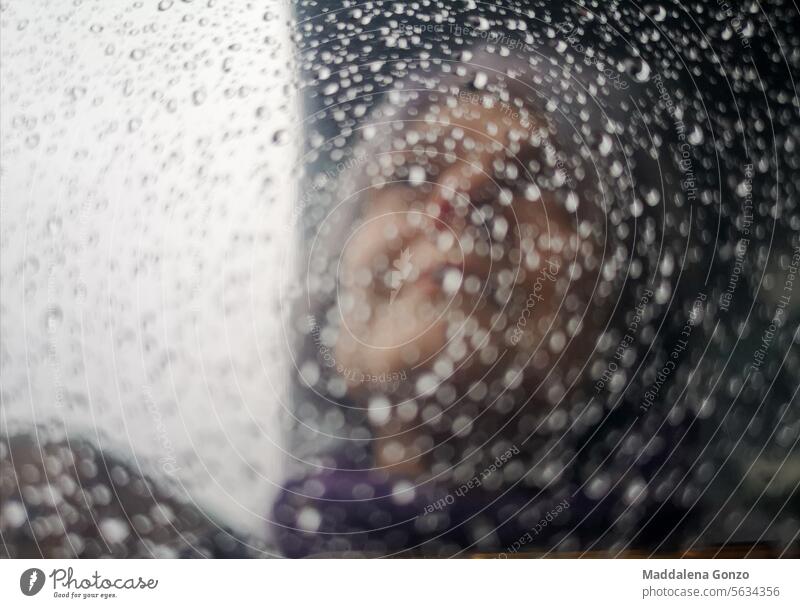 blurred reflection of a woman's face on a mirror covered with droplets blurry wet raindrops light dark out of focus drops of water weather rainy weather damp