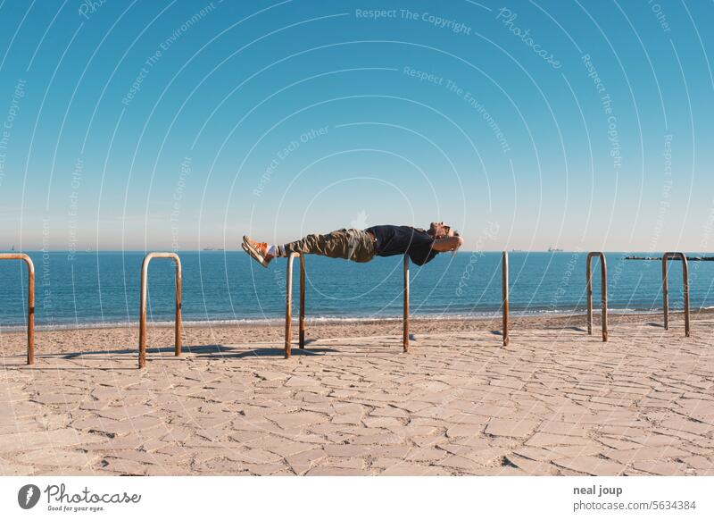 Mann liegt als Planke bequem über zwei Fahrradbügel und optisch auf dem Meereshorizont paradox widerspruch Entspannung Yoga starr stabil Spannung Kraft Erholung