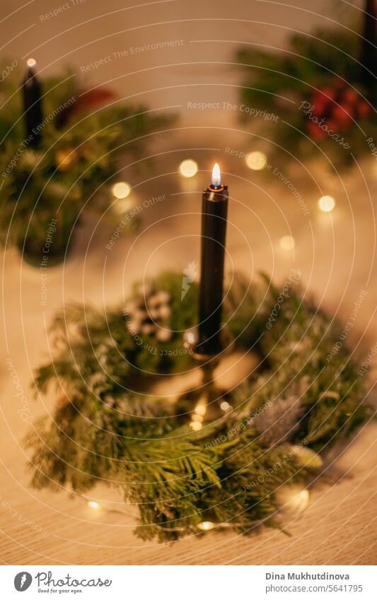 Christmas floral arrangement wreath with black burning candle. Centerpiece festive decoration with conifer branches and red berries. candles lights centerpiece