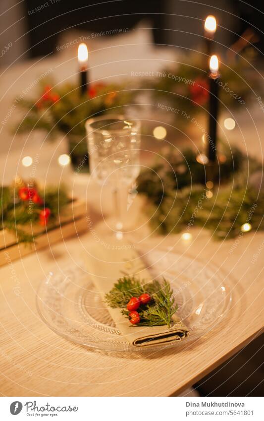 Christmas floral arrangement table setting with burning candle, glass and napkin. Centerpiece festive decoration with conifer branches and berries. candles