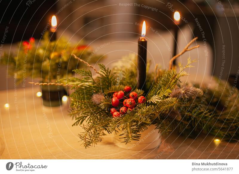 Christmas floral arrangement with burning candle. Centerpiece festive decoration with conifer branches and berries. candles lights centerpiece berry red