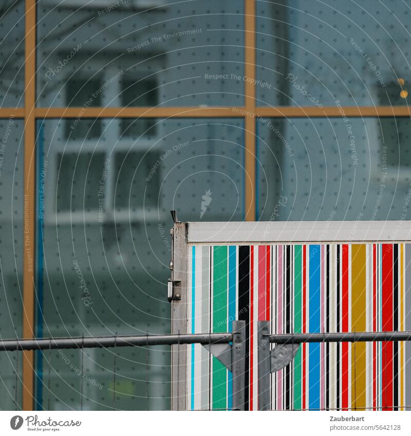 A container with colorful barcode stripes stands in front of a glass façade with geometric shapes, reflection Barcode variegated Stripe Container Facade Town