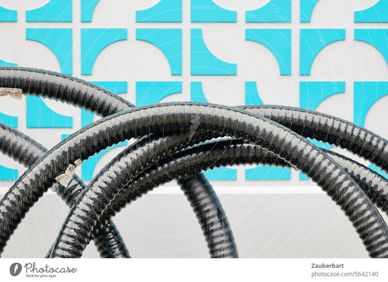 Black tubes in curves in front of a blue wall pattern Hose hoses Blue Pattern Abstract Contrast light blue Building materials Construction site Art installation