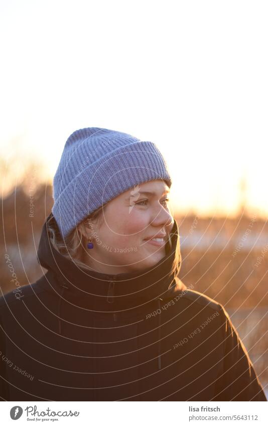 SUN IN WINTER - ENJOY - SMILE Woman 18 - 30 years Blonde Cap blue cap Winter winter jacket Warm light looking away Smiling Adults Colour photo Exterior shot