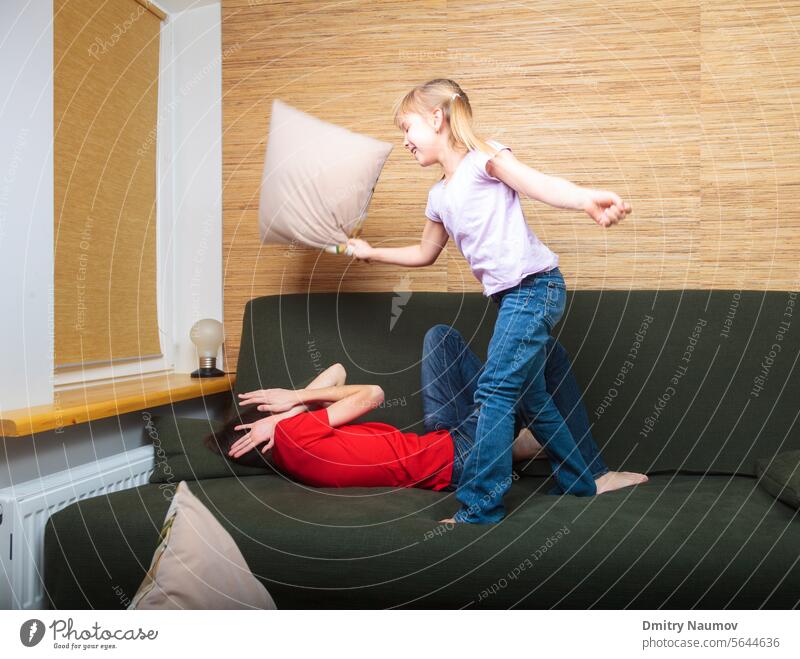 Siblings having pillow fight on a couch Half-sibling activity attack beat behavior boy brother child childhood children conflict defending defense enmity