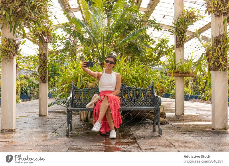 Woman taking a selfie on cellphone sitting on bench Botanical Garden woman chapultepec botanical garden smartphone greenhouse mexico tourist relaxation greenery