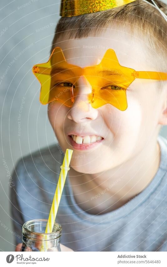 Young boy enjoying a drink with star sunglasses child smile new year's playful star-shaped drinking straw fun cheerful happiness party celebration costume
