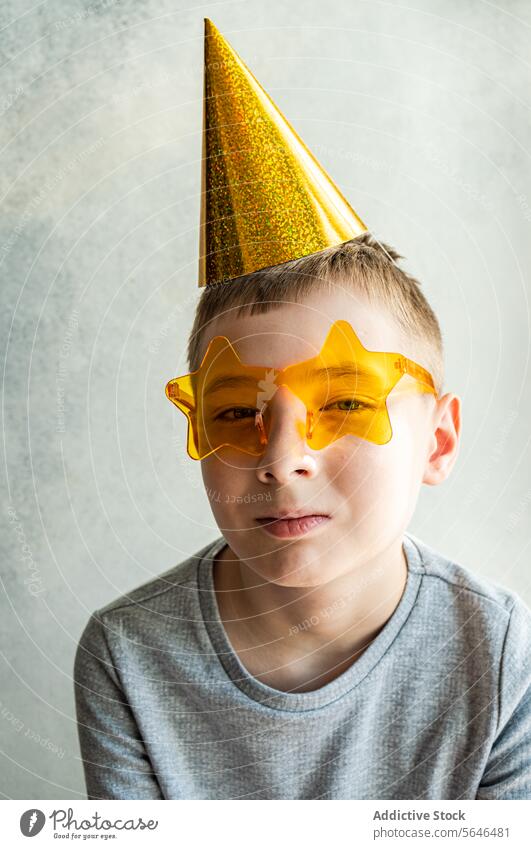 Boy with party hat and star-shaped glasses on textured background boy new year's celebratory golden yellow sunglasses backdrop smile young neutral pose child