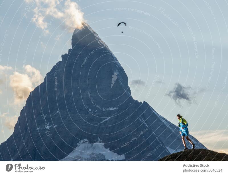 Adventurer Gazing at Paraglider Near Mountain Peak adventurer paraglider mountain peak sky dramatic awe observing vibrant attire distant soaring partly cloudy