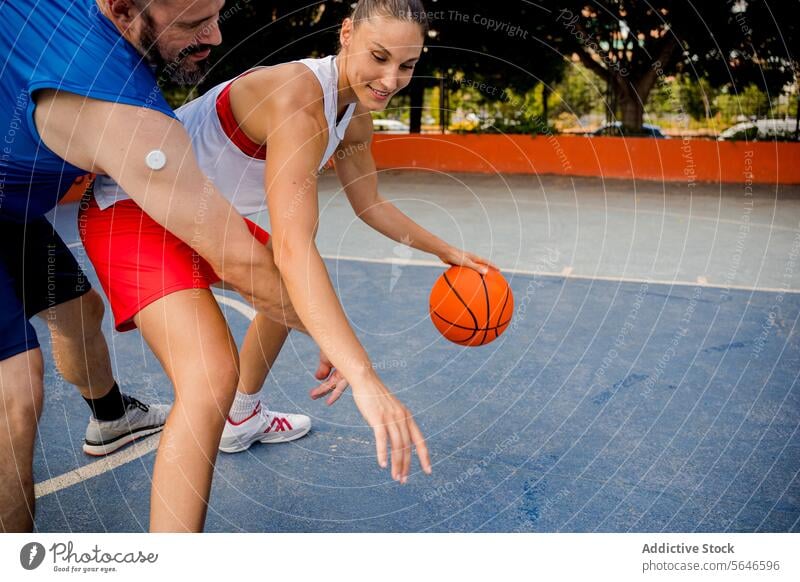 Determined man and woman in sportswear playing basketball on playground in city with buildings and trees in background Sportspeople Play Basketball Ball Defend