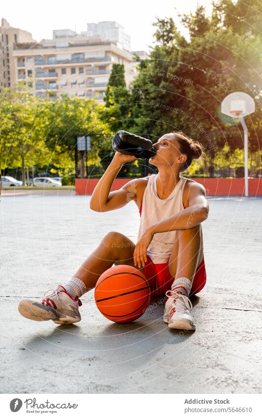 Sportswoman drinking water after playing basketball on court Drink Water Bottle Basketball Player Sports Ground Ball Rest Hydrate Woman Playground City Young