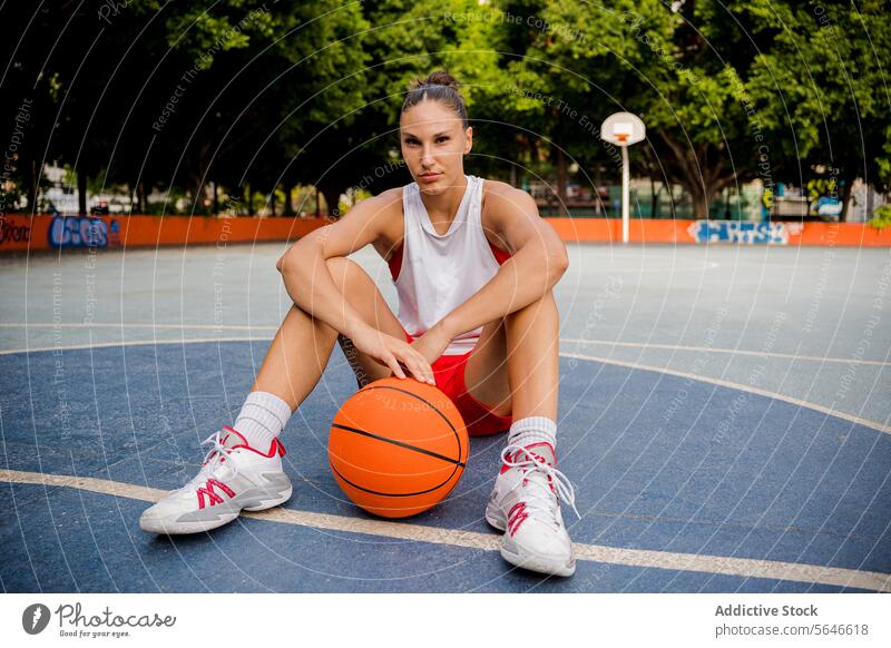 Confident woman sitting with basketball on playground Sportswoman Basketball Ball Court Sporty Player Relax Athlete Woman Sports Ground Activewear Training